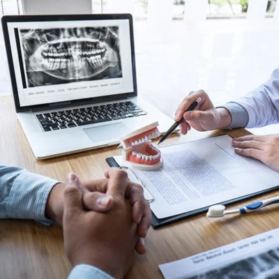 Two people at a desk discuss dental care using a model of teeth.